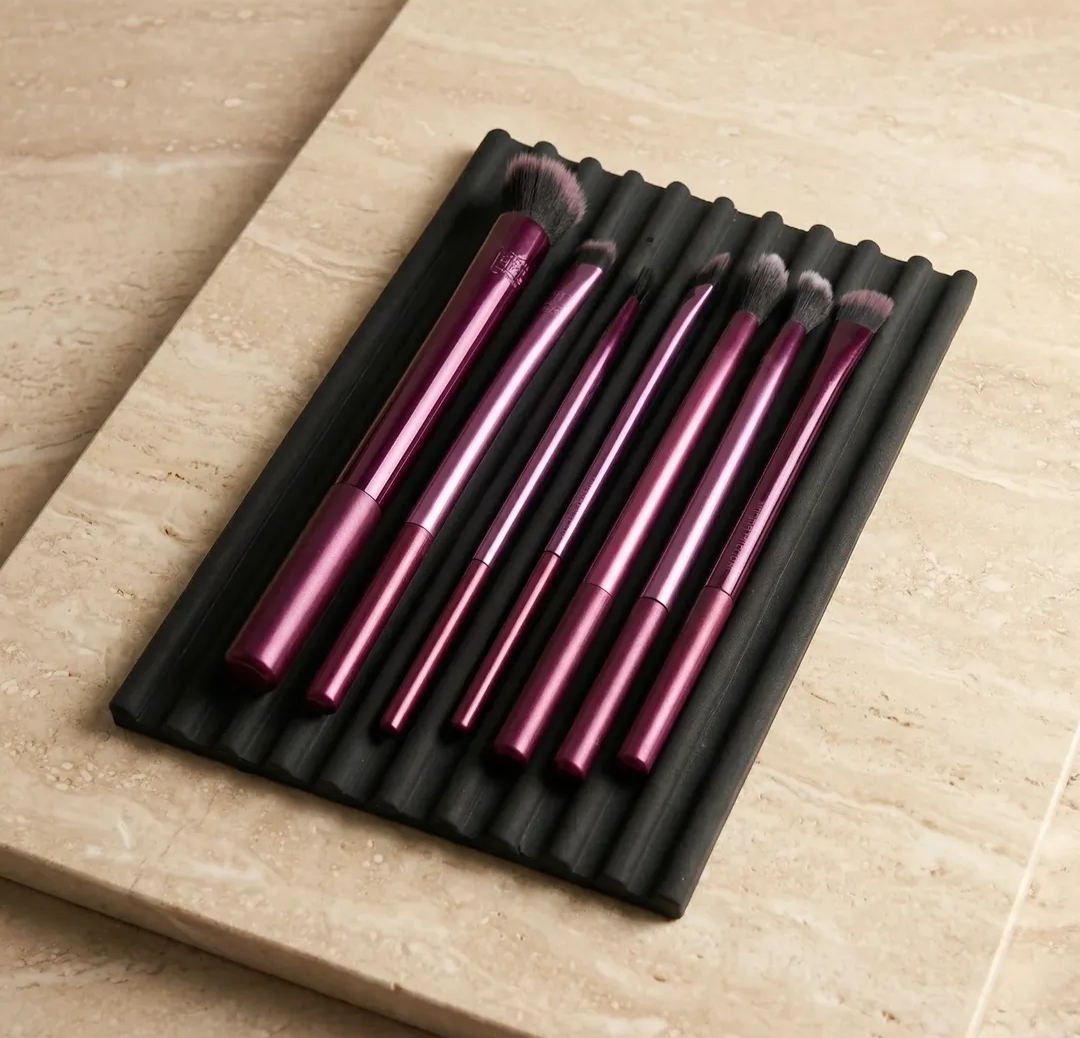 Matte black ribbed makeup brush rest holding a set of pink brushes on travertine